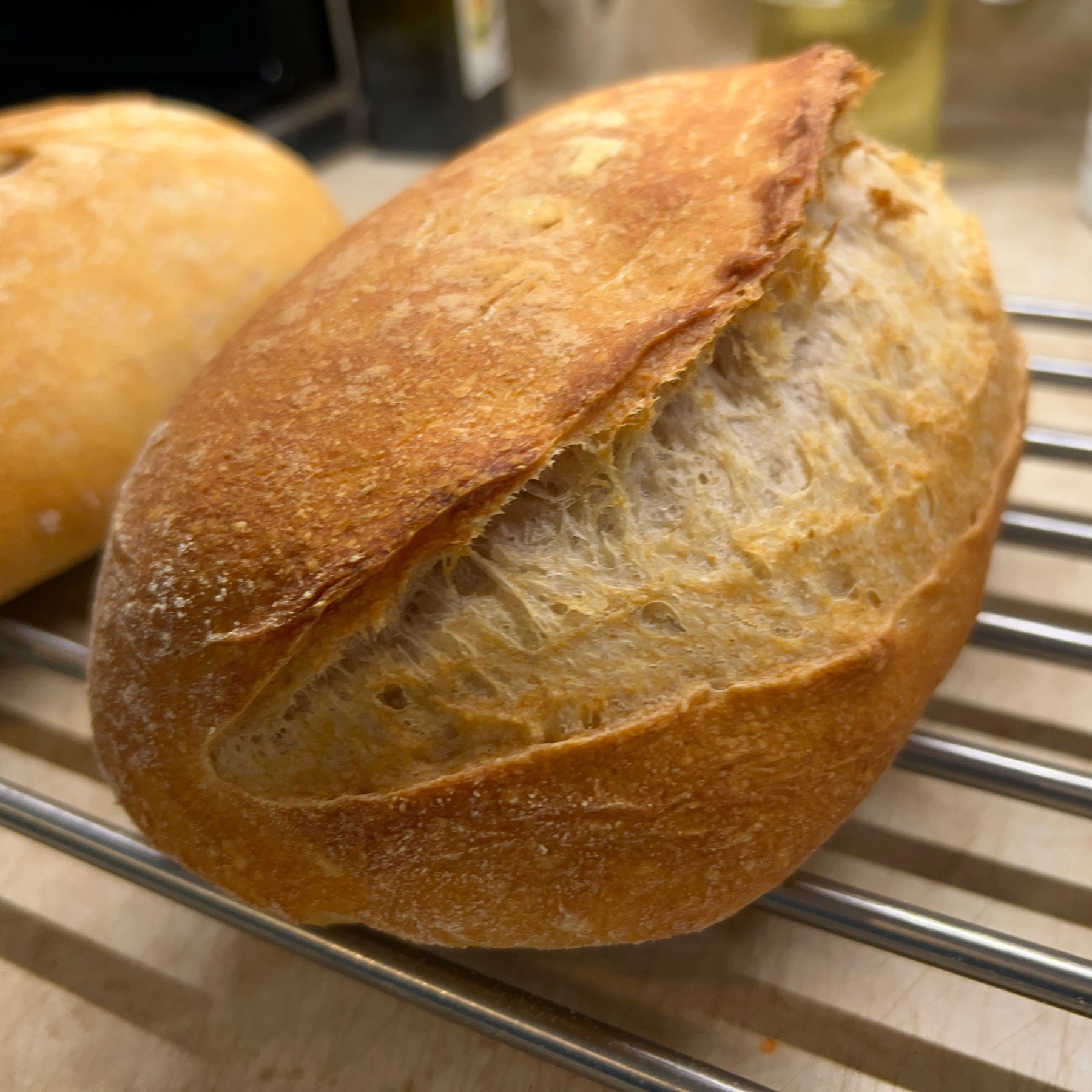 Sourdough bread loaf with slash in it cooling on metal rack. 