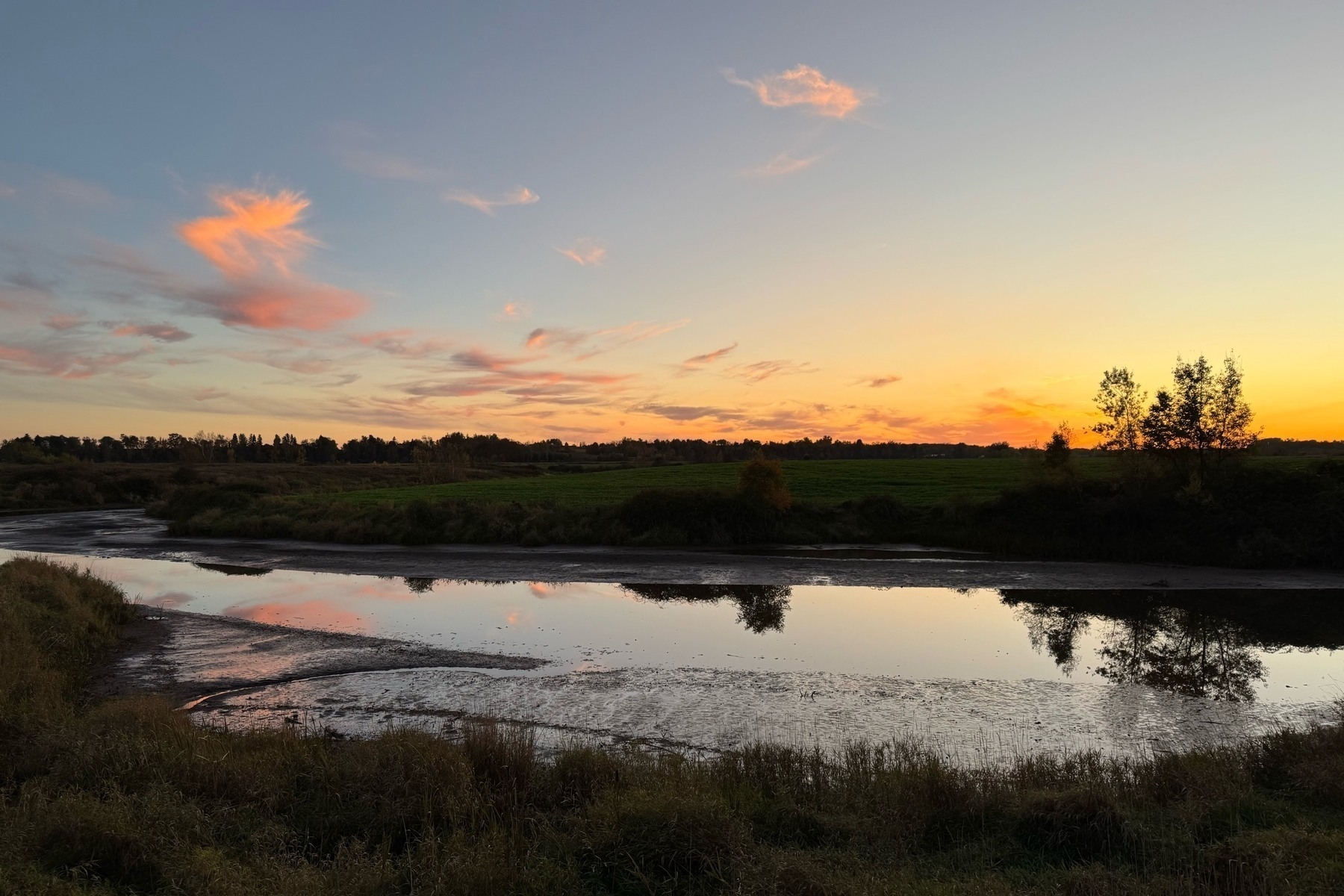 Winding stream with orange and blue sky with clouds reflected in it at sunset. 