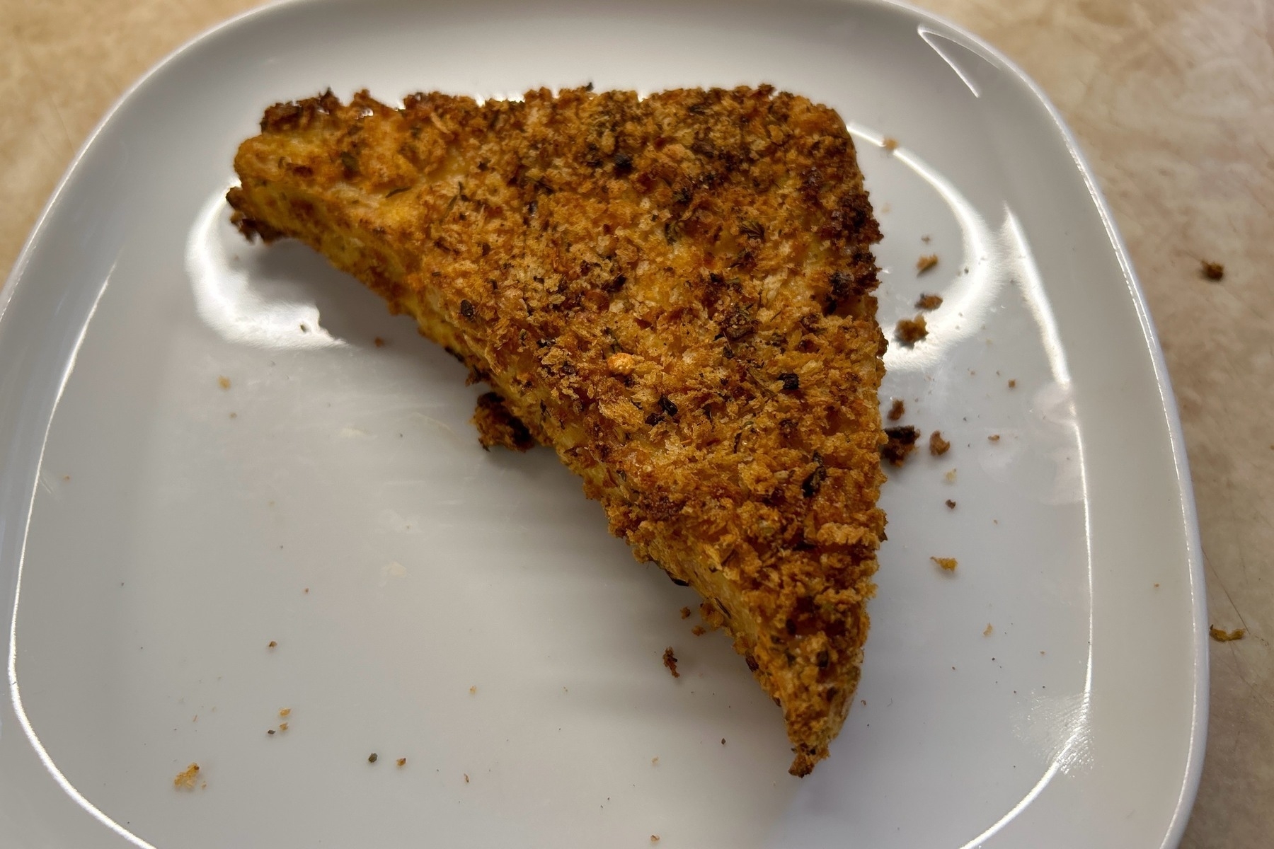Triangle of breaded and baked tofu on a square white plate. 