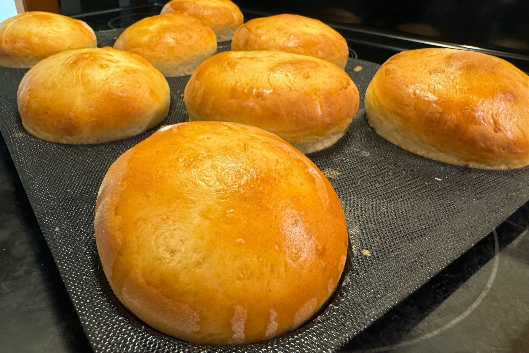 Golden hamburger buns sitting on a baking tray at an angle. 
