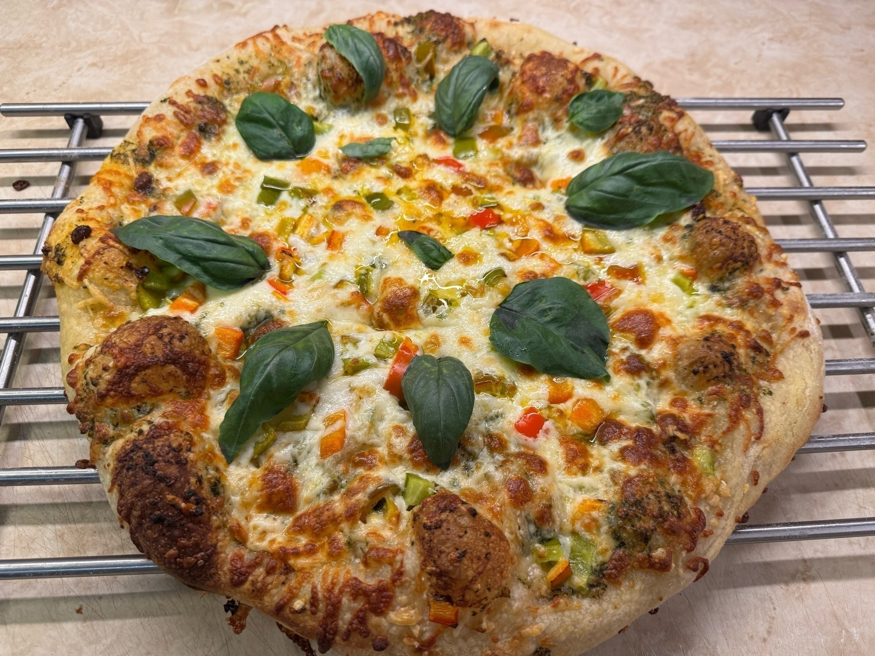 Cheese pizza on a metal rack with basil leaves on top.