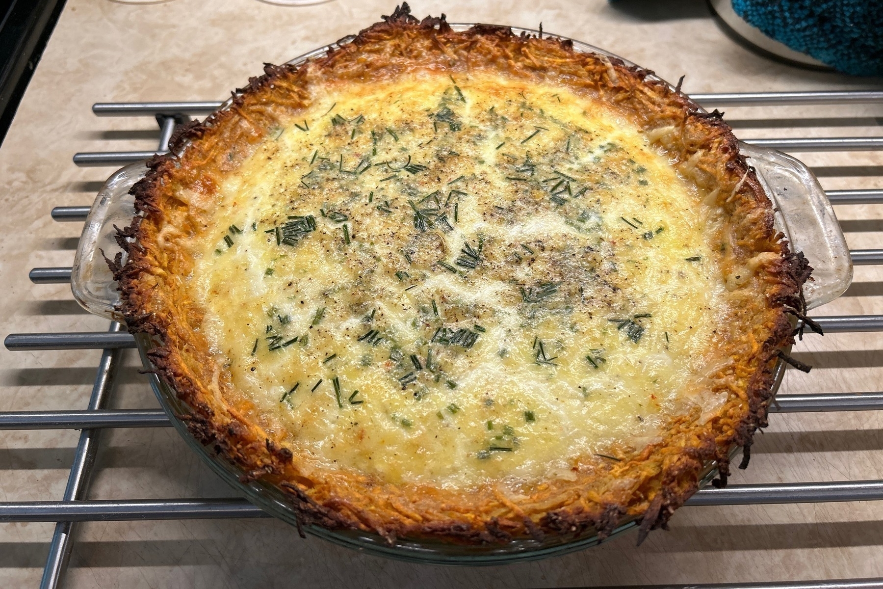 Quiche in a glass pie dish cooling on a metal rack. 