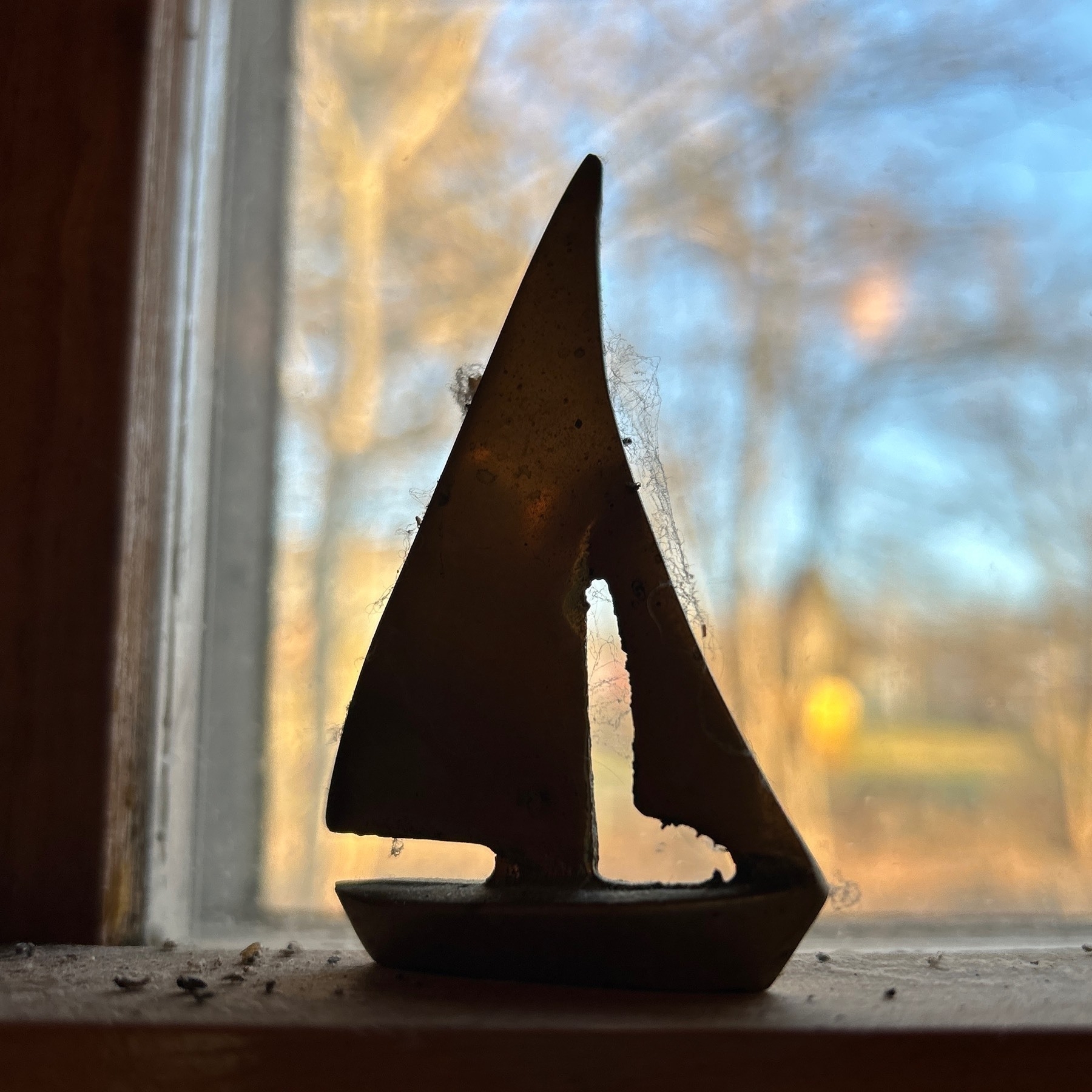 Tiny metal schooner ornament on a window shelf. 