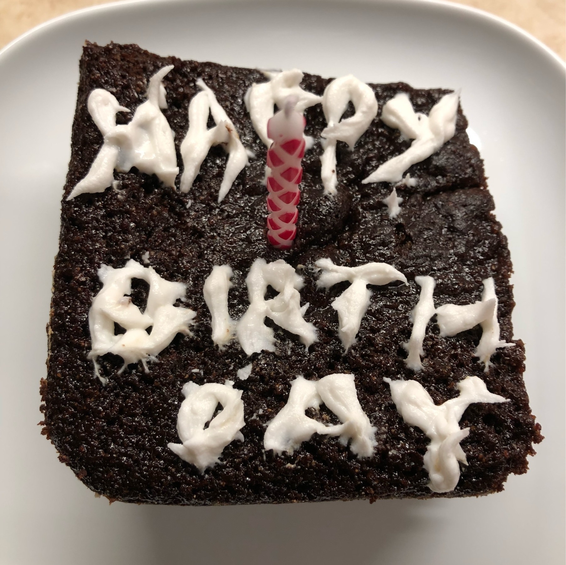 Chocolate brownie with candle and icing spelling out happy birthday.