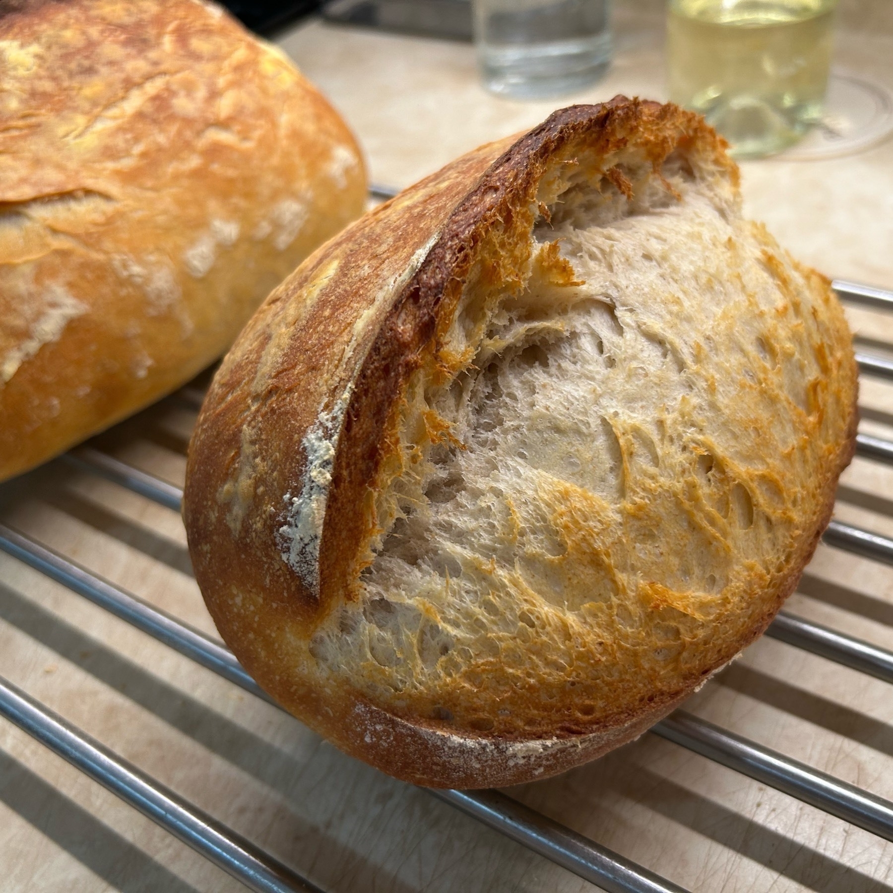 A rustic loaf of sourdough bread with a large slash where it expanded during cooking on top of a wire rack. 