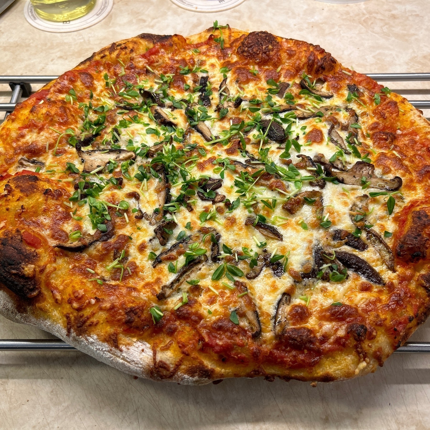 Cheese pizza topped with mushrooms and chopped pea shoots on a metal cooling rack. 