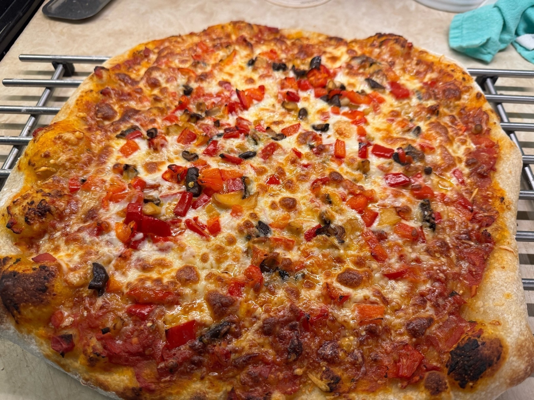 Cheese pizza with red peppers and mushrooms on a metal rack.