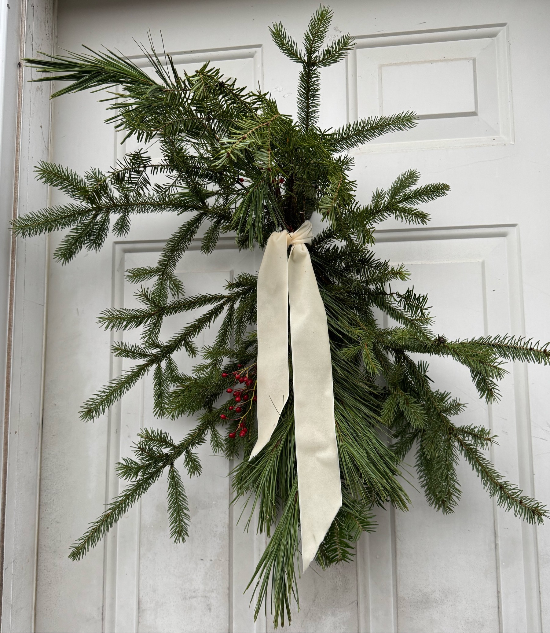 Bough of spruce branches attached to a white door. 