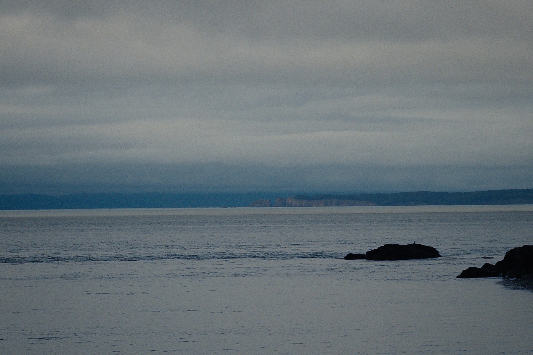 Greyish ocean with grey clouds above with a few rocks to the right. 