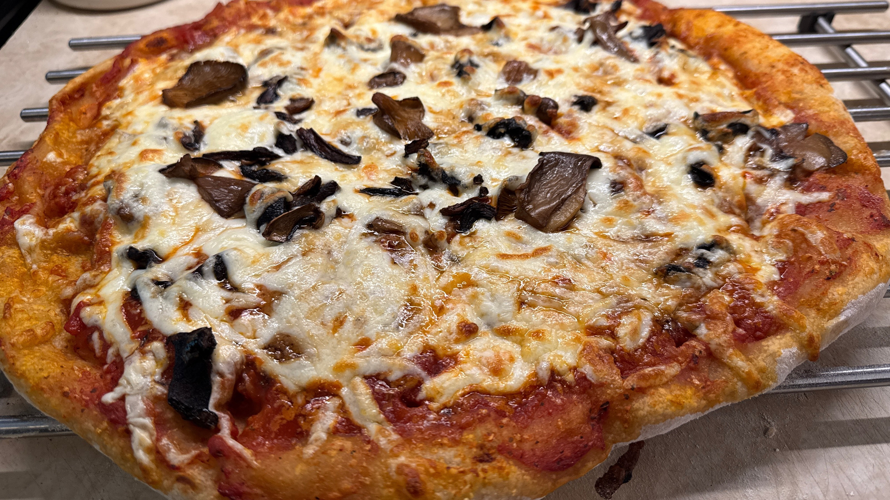 Pizza with mozzarella cheese and mushrooms on top sitting on a cooling rack. 