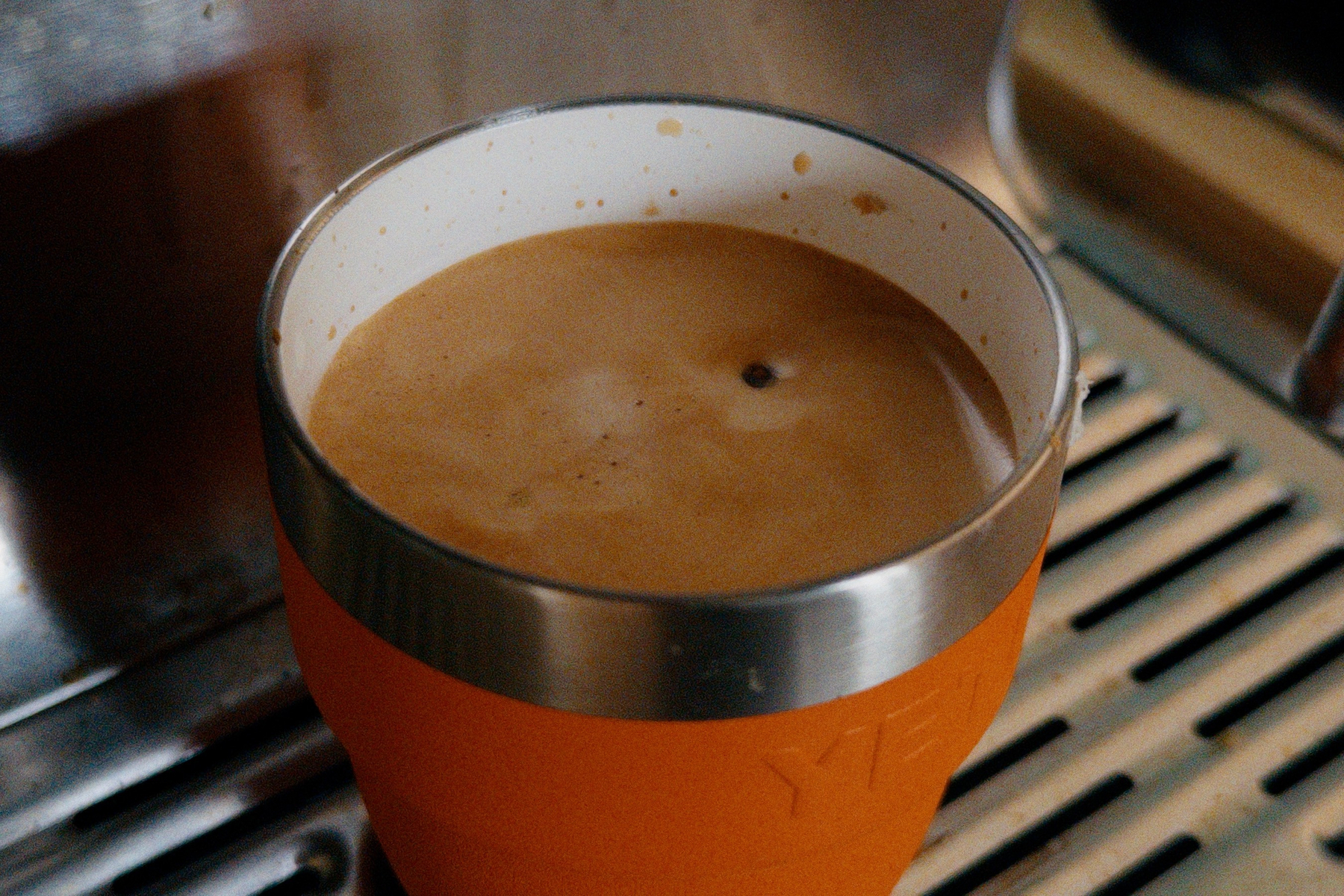 Espresso in an orange metal cup with a white interior on an espresso machine. 