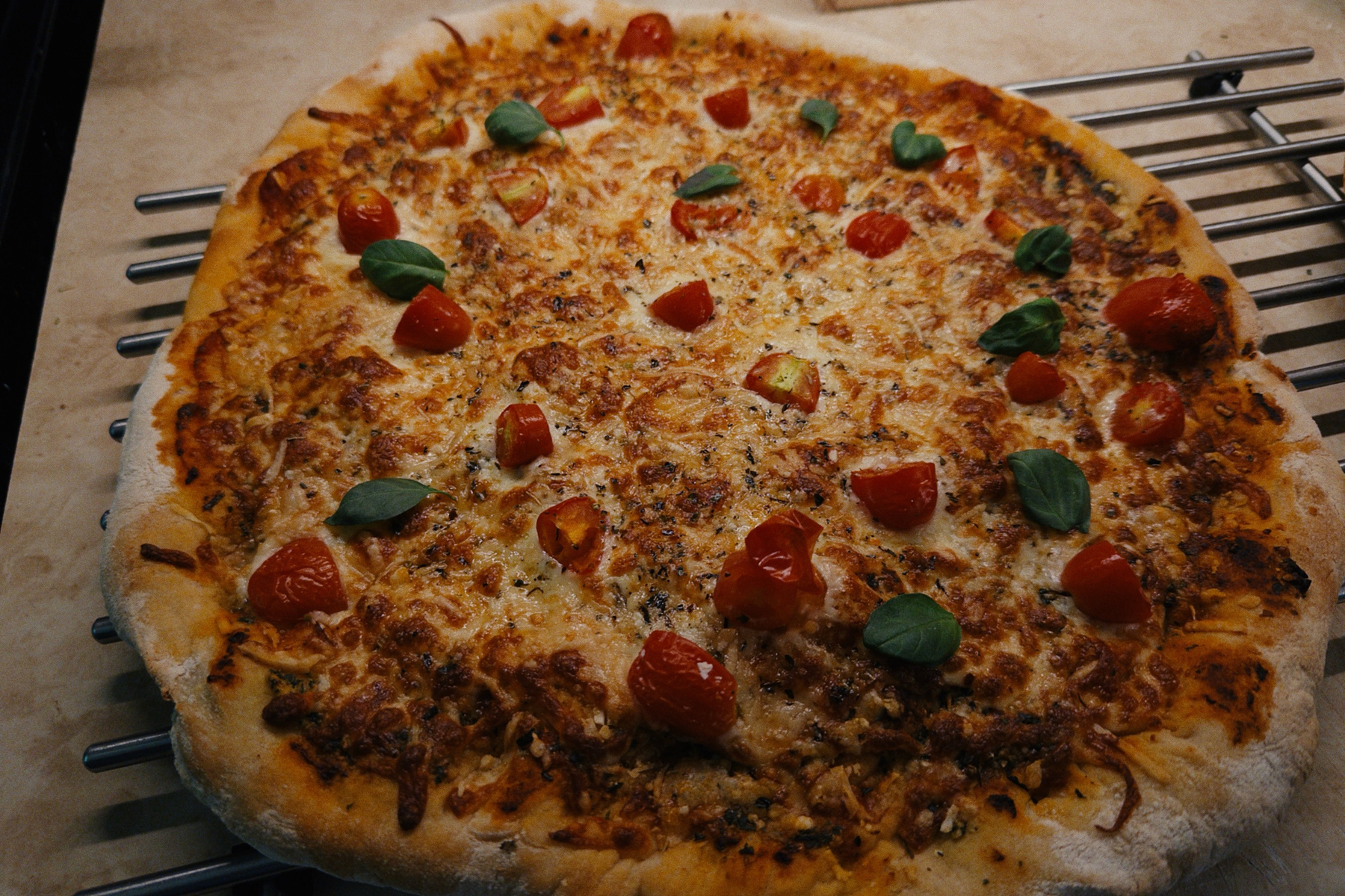 Cheese pizza on a cooling rack with small tomatoes and basil leaves on top of the cheese. 