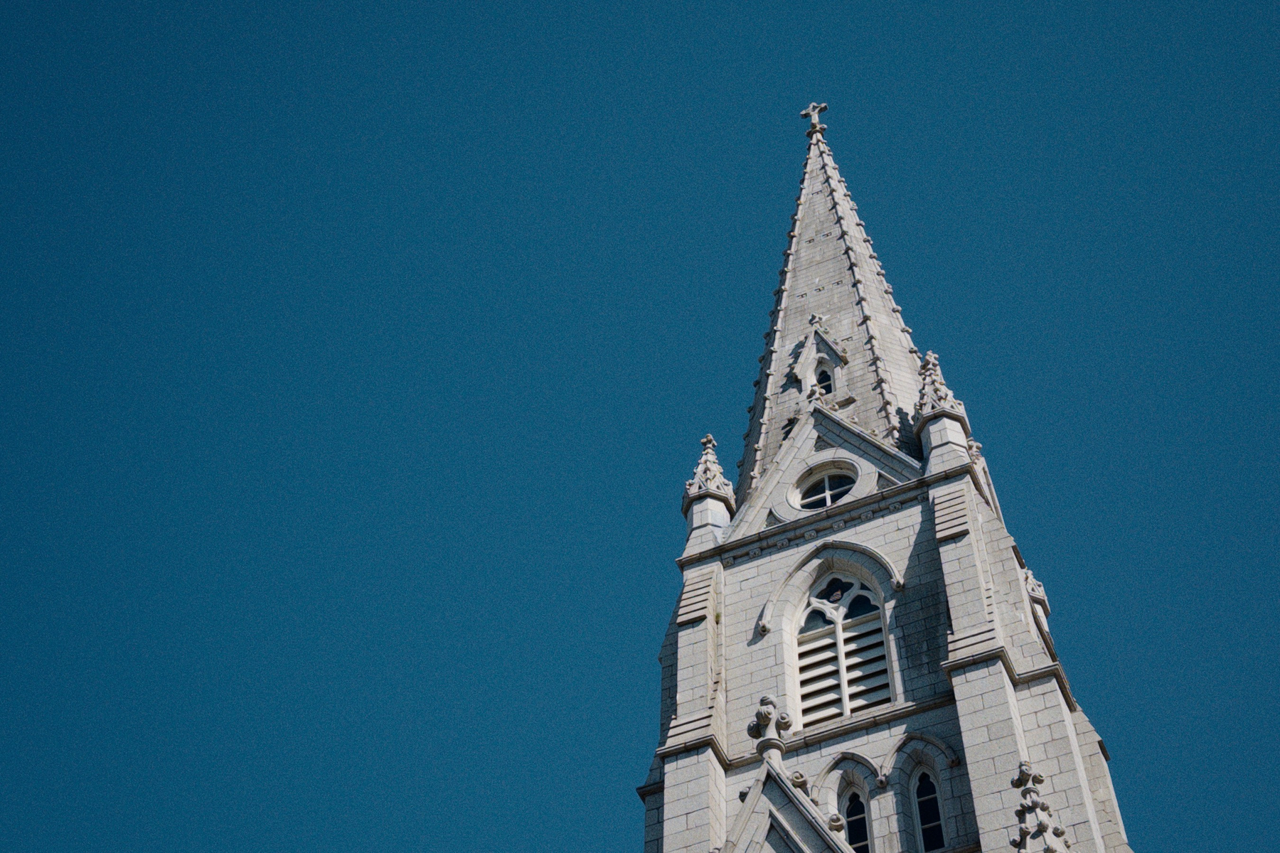Top of stone church spire with clear blue sky beside it. 