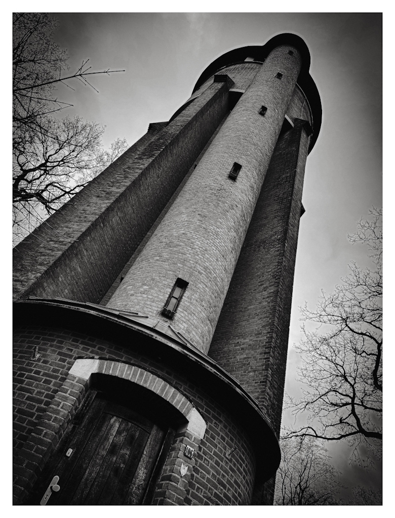 A water tower photographed from a frog perspective, diagonally placed in the image, in black and white. 