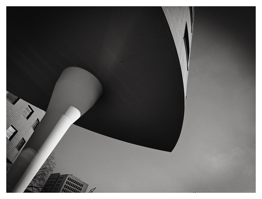 Extended part of a building resting on a white pillar. In black and white. 