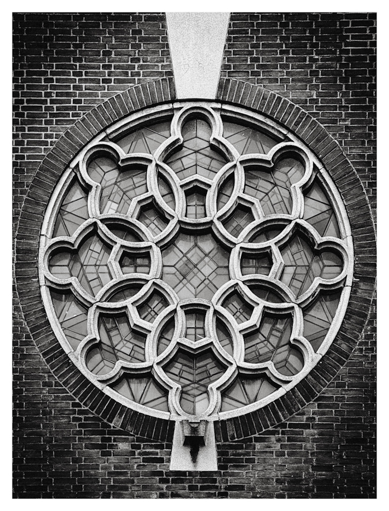 Round window with intricate pattern in a church wall, in black and white. 