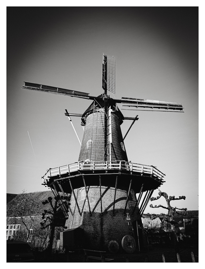 Windmill centered in de frame, against the backdrop of a blue sky, in black and white. 