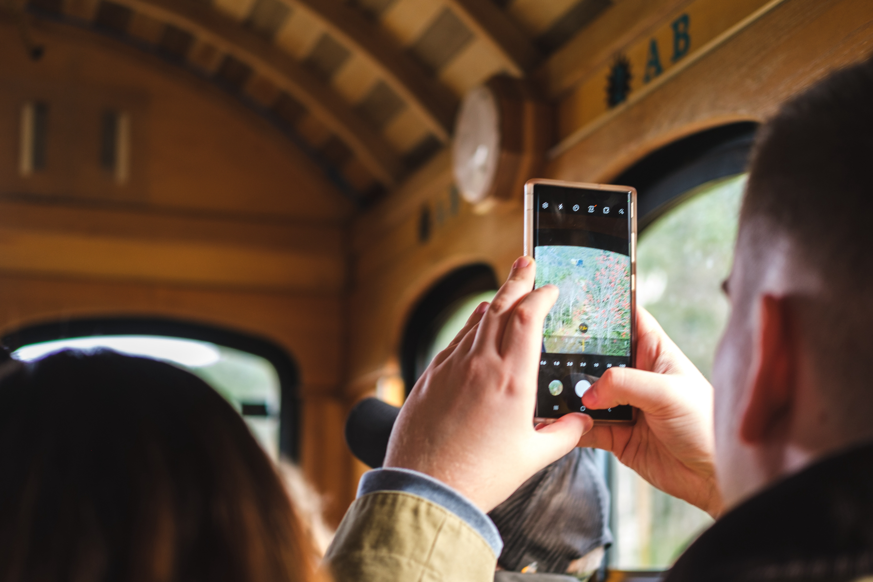 Over the shoulder photo of a person taking a smartphone photo inside a train carriage, capturing the view outside the window.