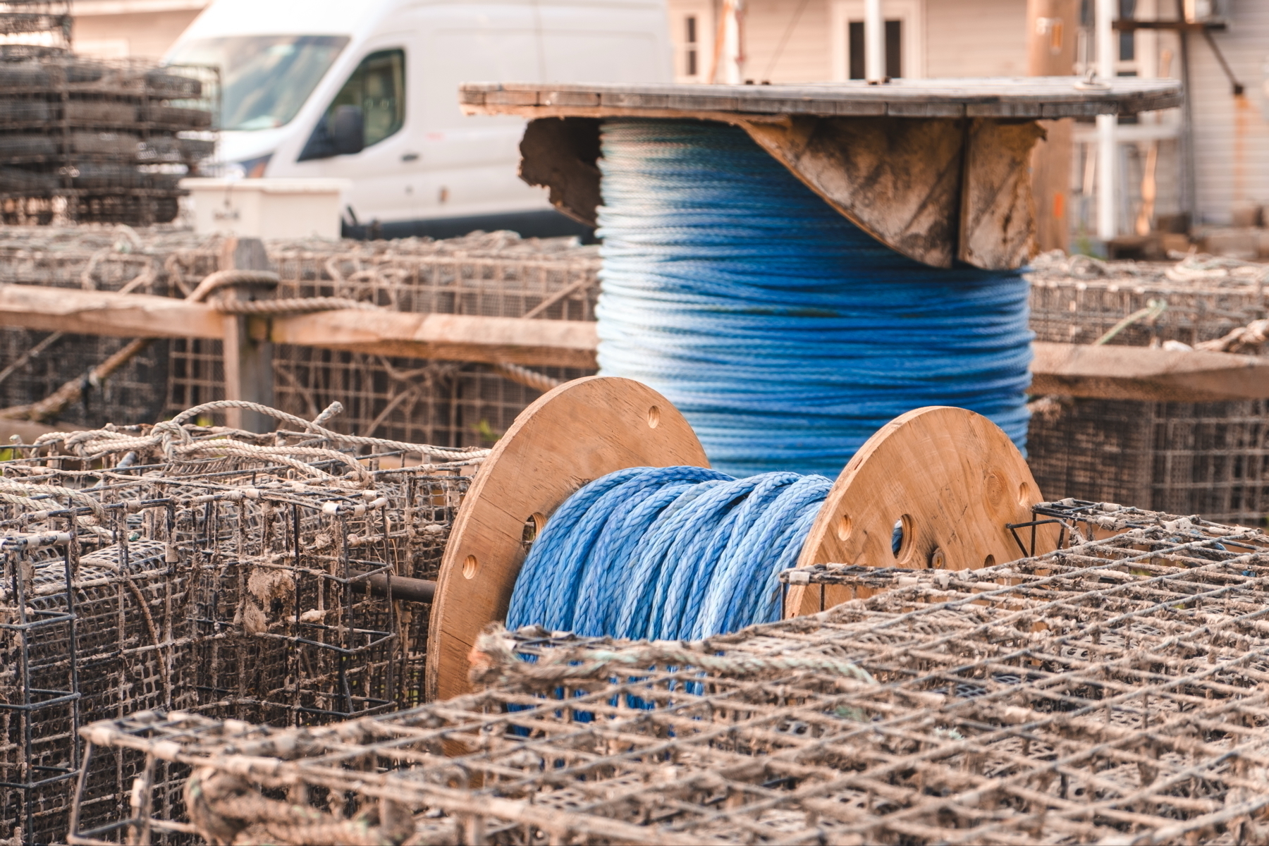 Two large wooden spools of blue rope are surrounded by stacked wire lobster traps.