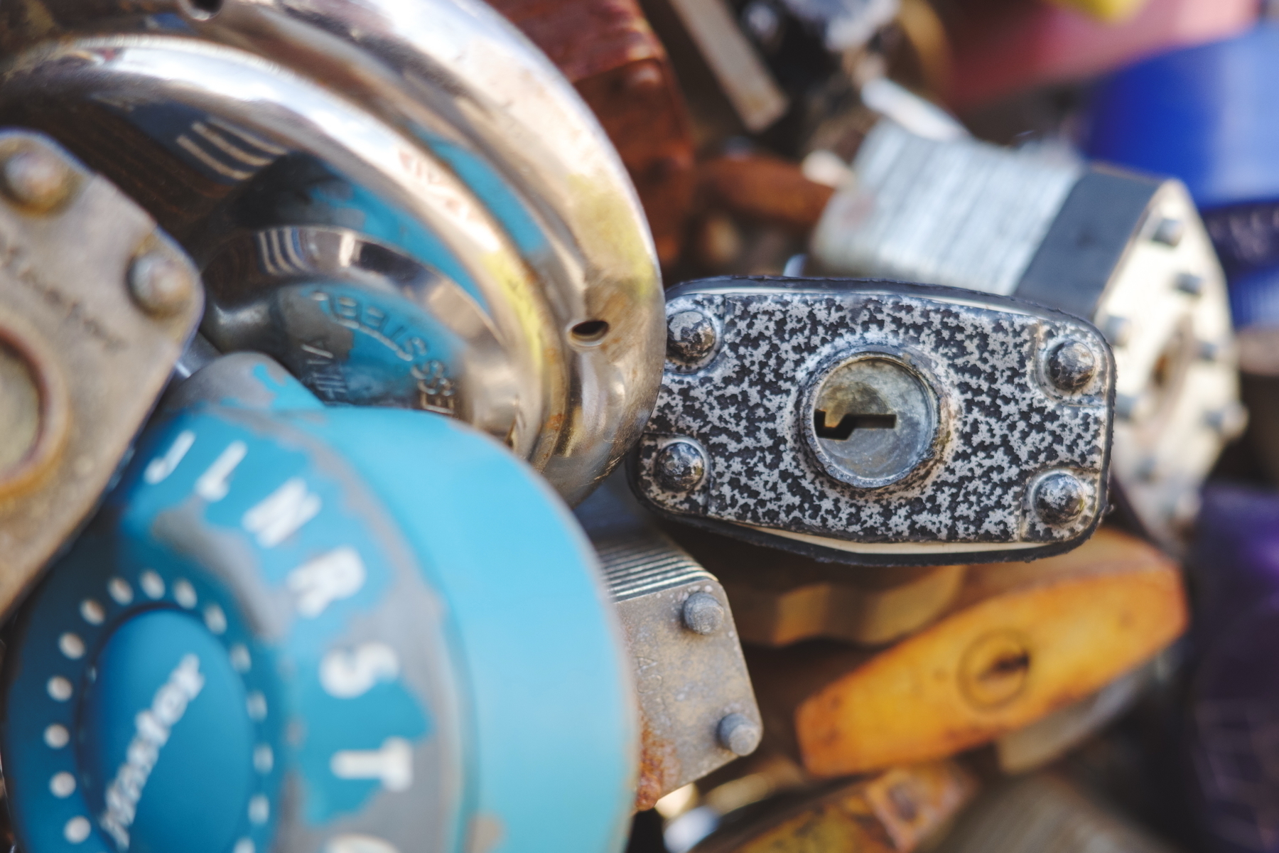 Close-up of assorted padlocks and combination locks, including a blue dial lock and a textured metal key lock, arranged together.