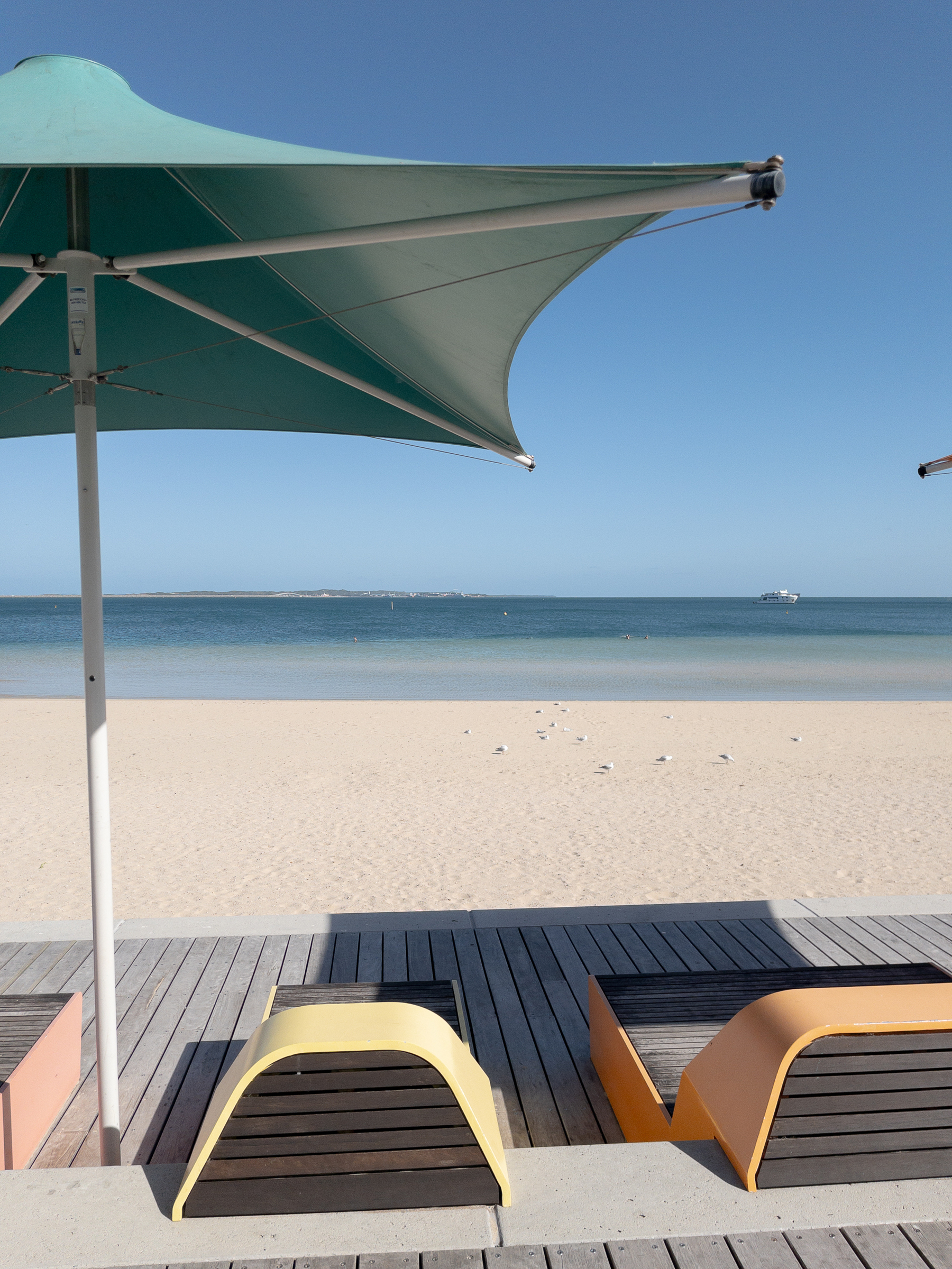 Auto-generated description: Beach scene with lounge chairs under umbrellas on a wooden deck facing a calm sea.