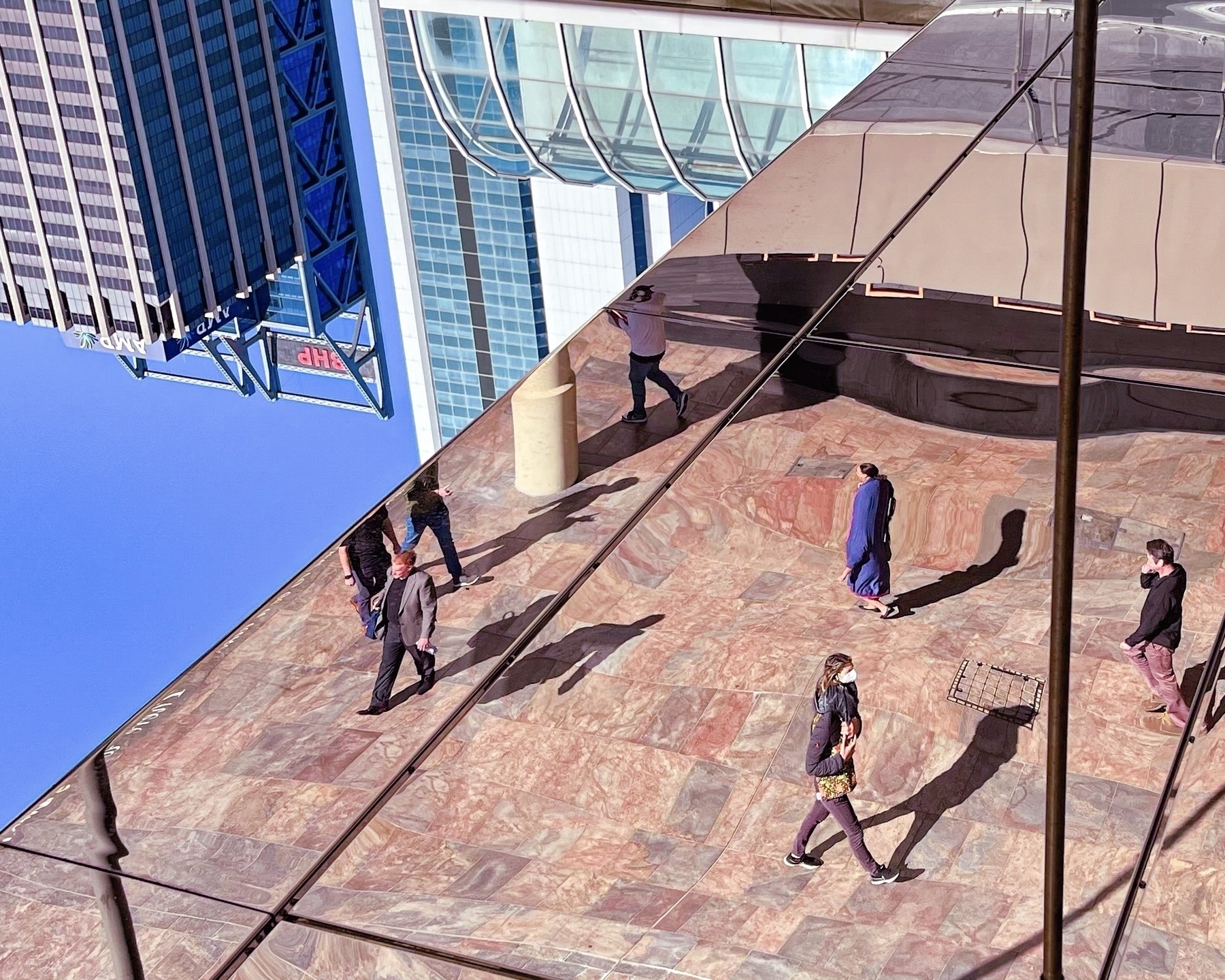 Auto-generated description: People are walking on a tiled surface with reflections creating an intriguing visual effect.