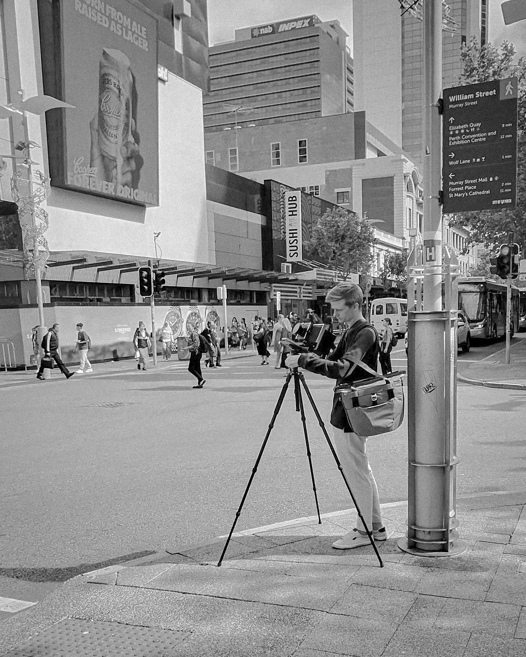 Auto-generated description: A person is setting up a camera on a tripod at a city street intersection.