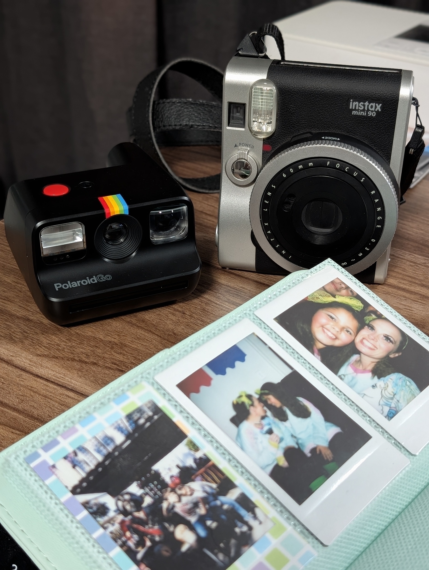 Auto-generated description: Two instant cameras are placed beside an open photo album displaying polaroid pictures.