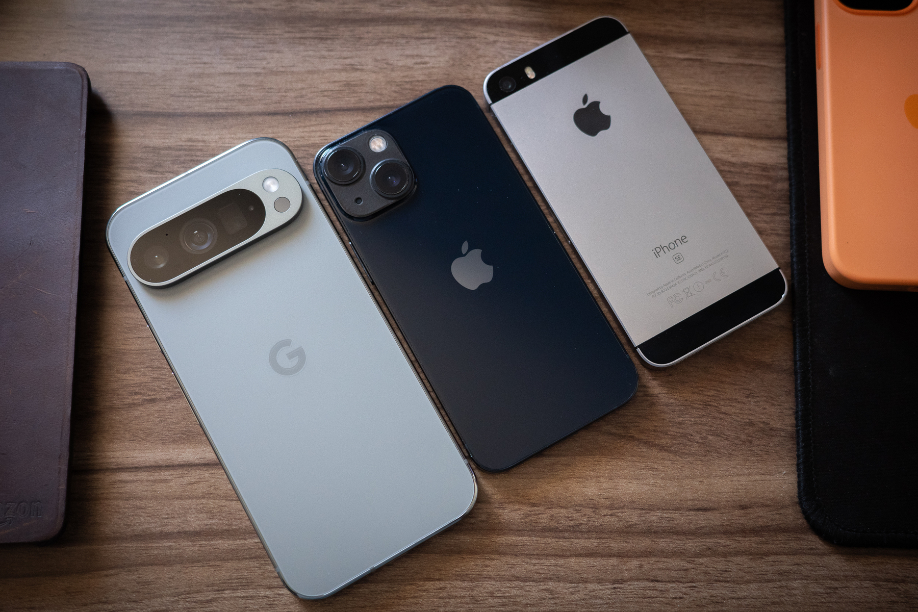 Auto-generated description: Three smartphones, including a Google Pixel and two iPhones, are placed side by side on a wooden surface.