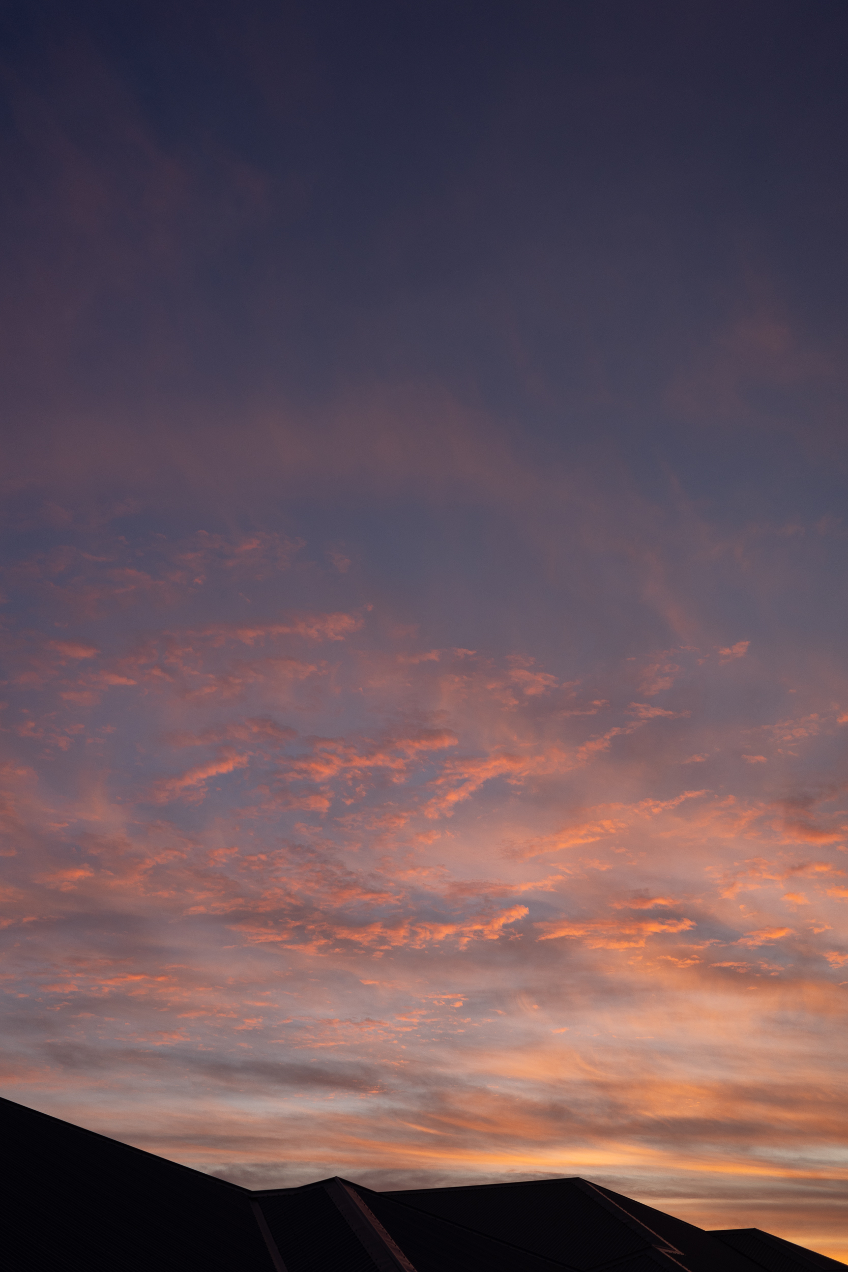 Auto-generated description: A twilight sky with hues of orange and purple is seen above silhouetted rooftops.