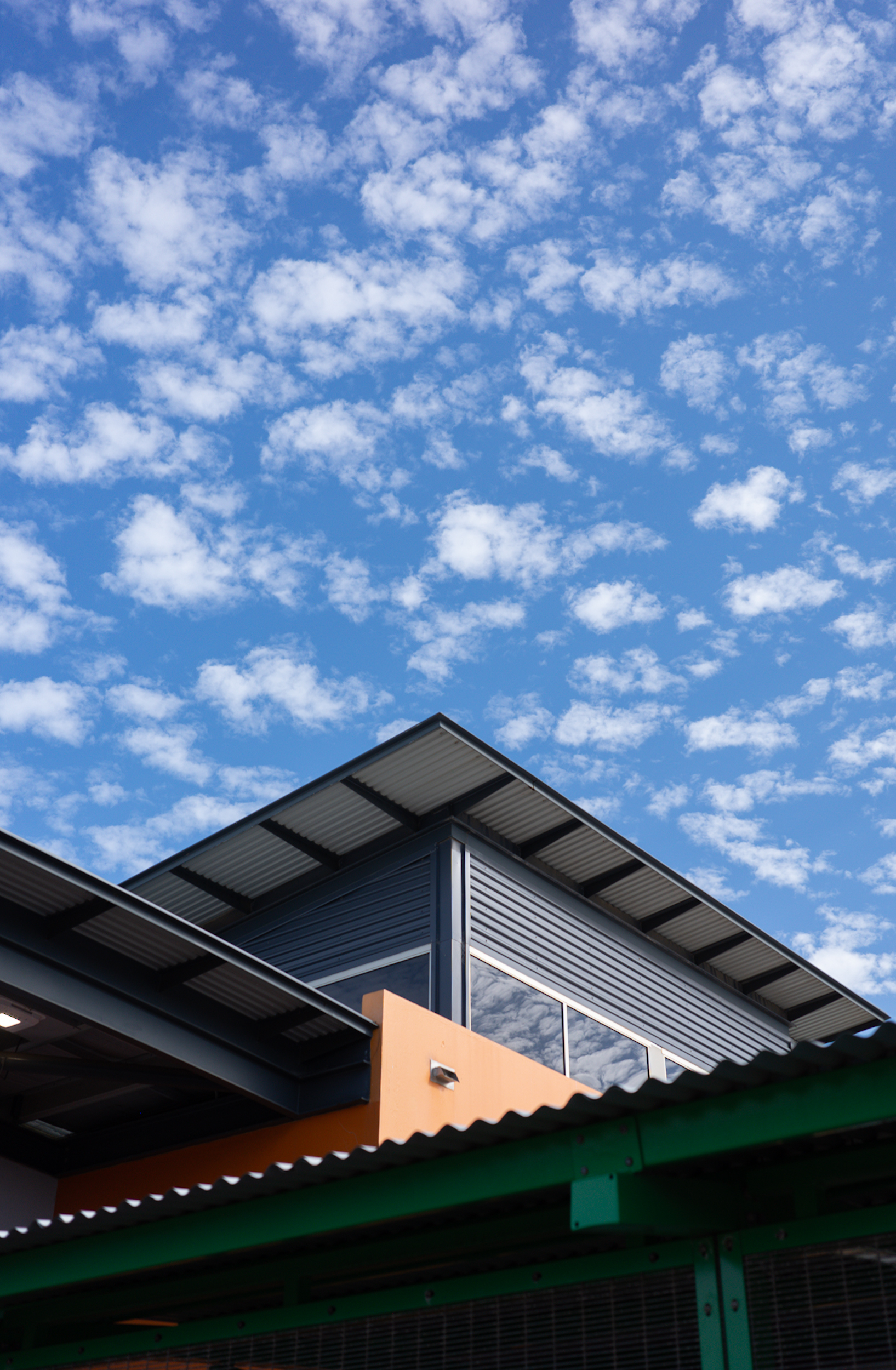 Auto-generated description: A modern, angular building with metal siding is set against a sky filled with scattered white clouds.