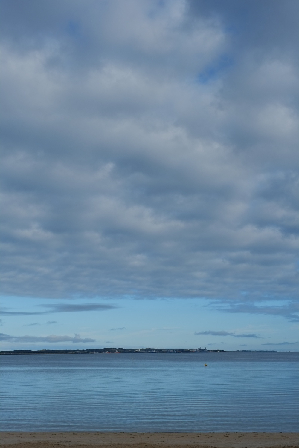 A calm beach scene with a tranquil sea under a sky filled with scattered, fluffy clouds.