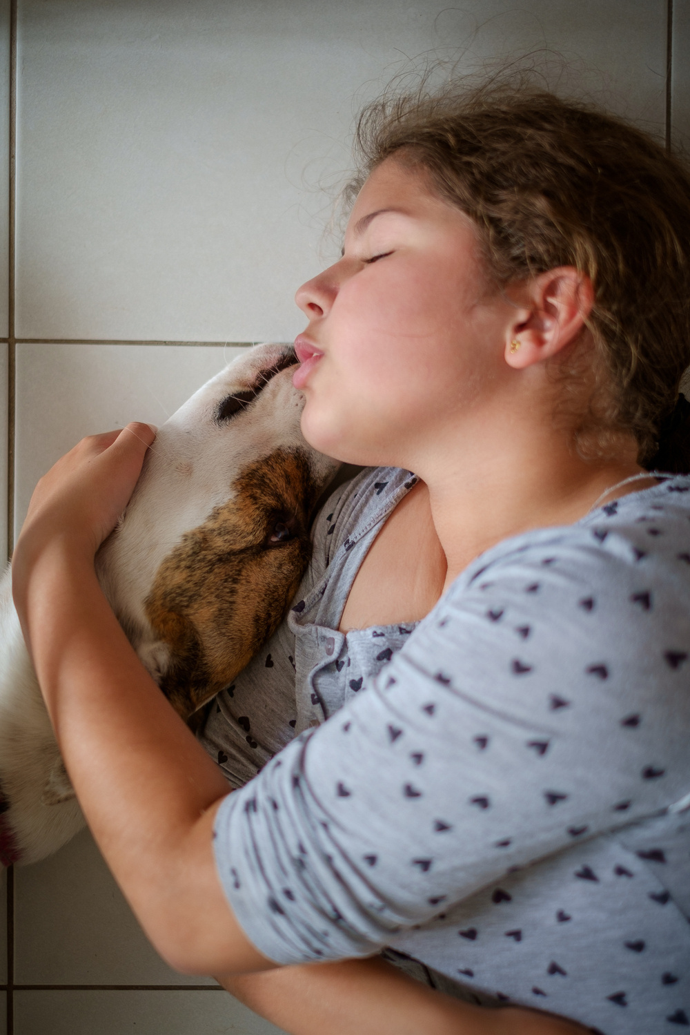 A girl is lying on the floor, lovingly embracing a dog.