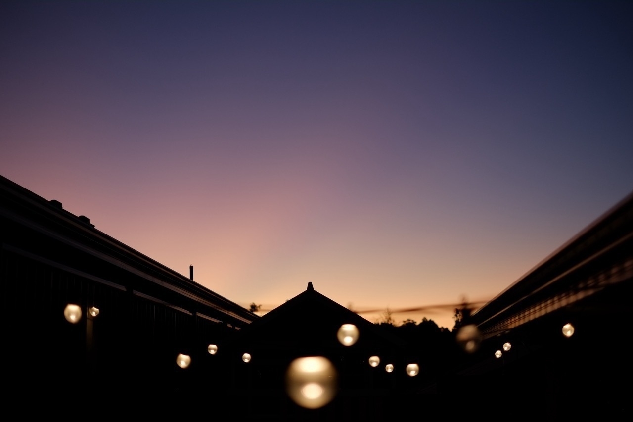 A row of bokeh lights glows against a twilight sky with silhouetted rooftops.