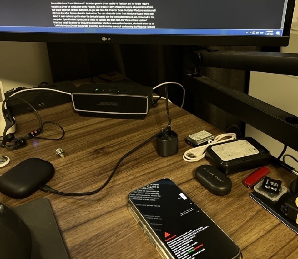 Auto-generated description: A desk setup featuring an LG monitor, smartphone, Bose speaker, and various tech items and accessories on a wooden surface.