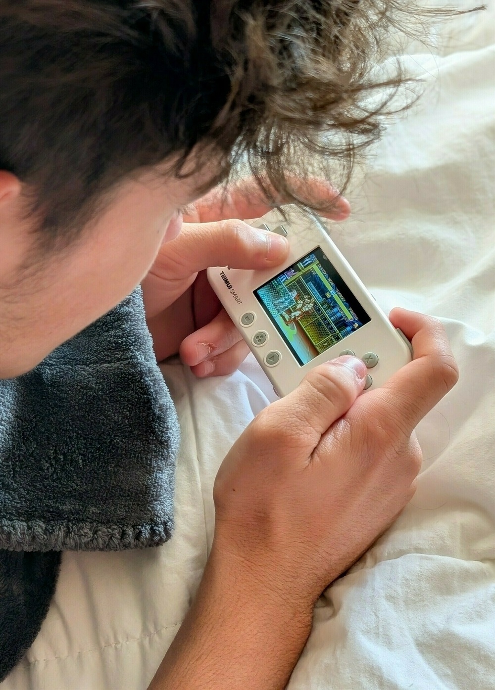 A person is playing a retro-style game on a white handheld gaming device.