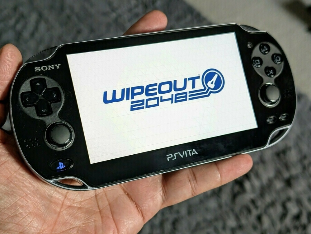 A Sony PS Vita handheld console displays the game Wipeout 2048 on its screen.