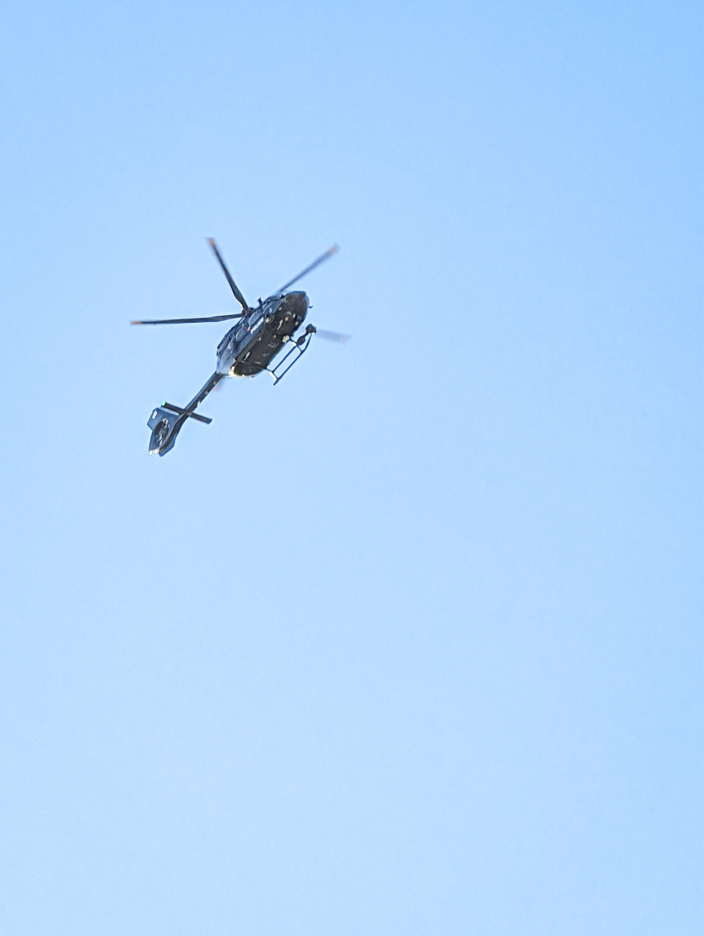 A helicopter is flying against a clear blue sky.