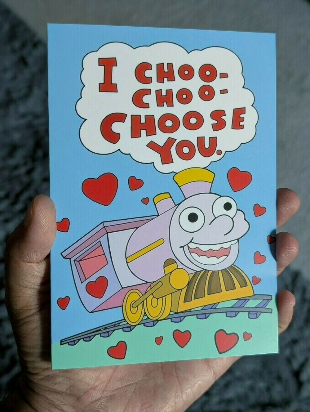 A cartoon train with hearts around it and the text I choo-choo-choose you is depicted on a greeting card.