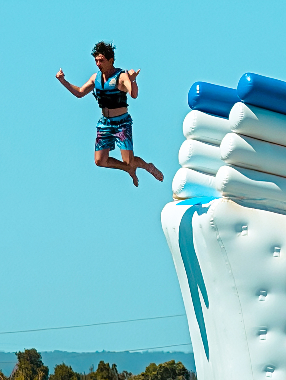 A person wearing a life vest is caught mid-air in a jumping pose from an inflatable water structure.