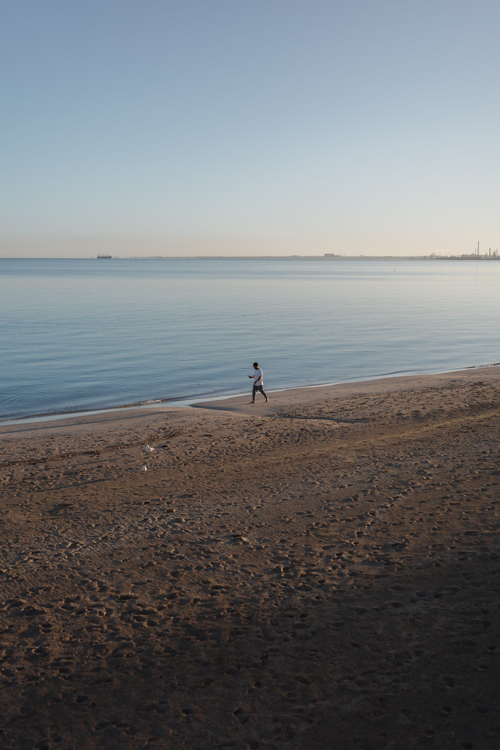 Auto-generated description: A person is jogging along a calm beach at sunrise or sunset, with the ocean and a distant shoreline in the background.