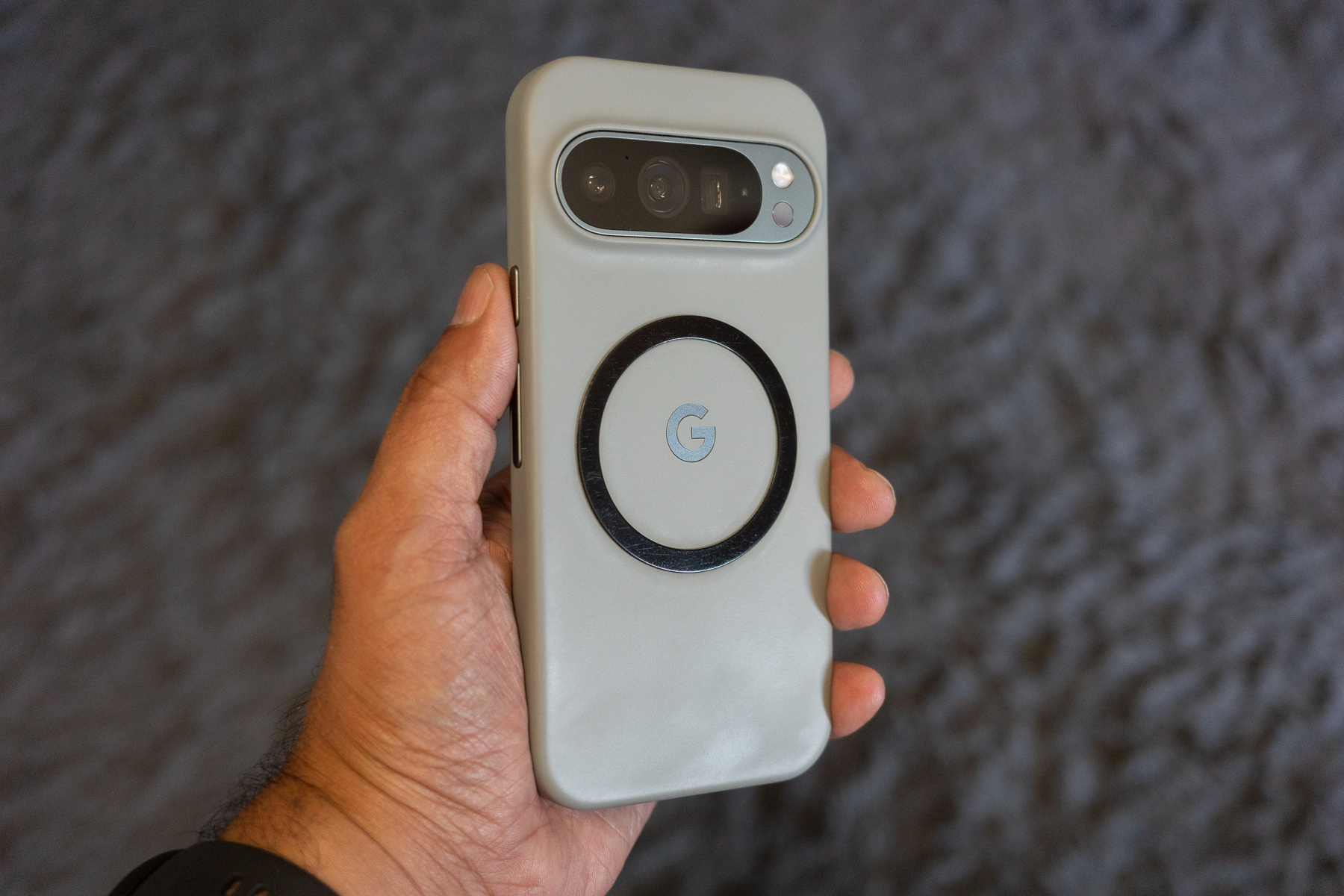 Auto-generated description: A person is holding a smartphone with a gray case featuring a circular design and a G logo on the back.