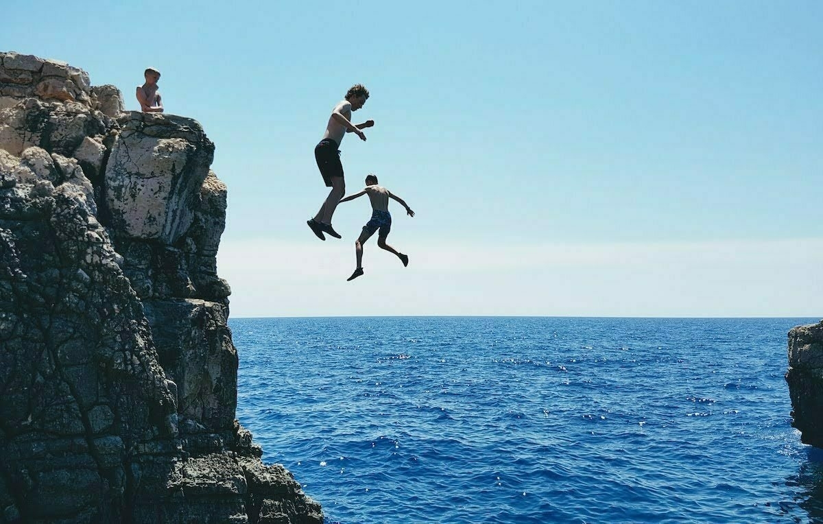 two boys jumping off a cliff into the ocean