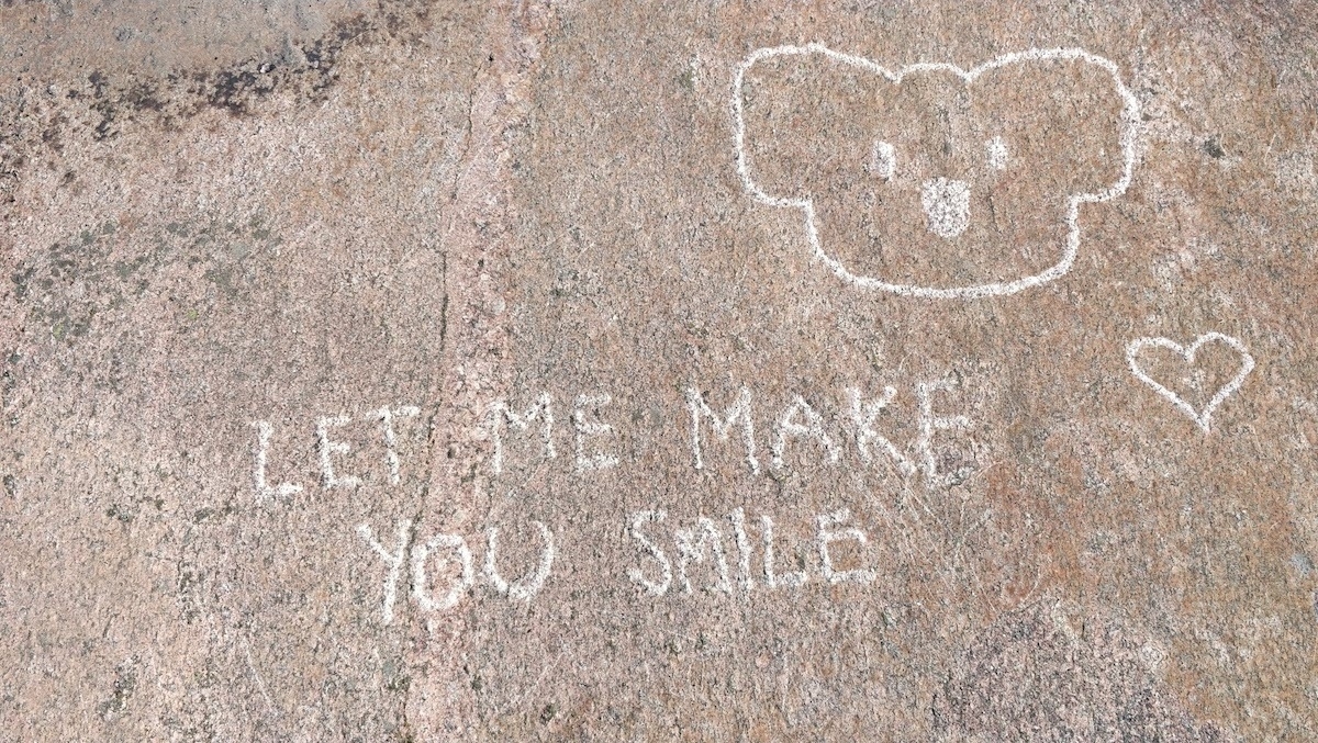 graffiti on a rock by the coast saying 'let me make you smile'