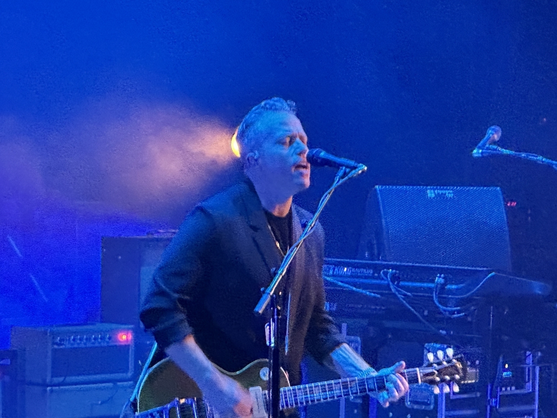 A close up photo of Jason Isbell singing and playing the guitar