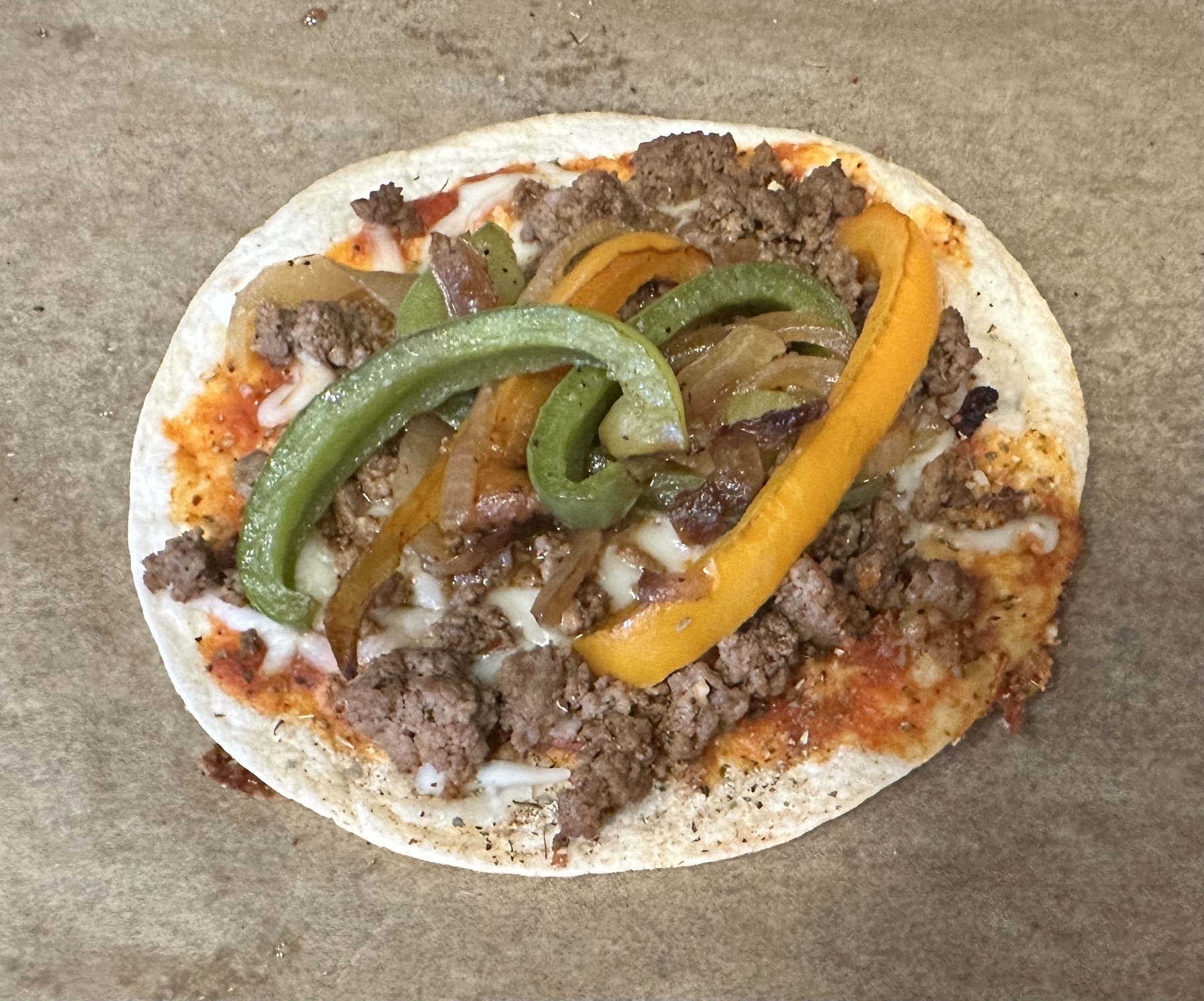 A cooked tortilla pizza topped with ground beef, veggies, and cheese.