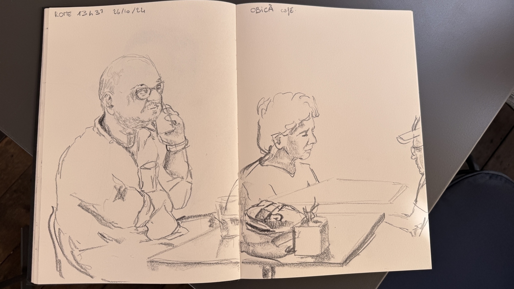 A sketch of me in an artist’s notebook. I am talking on the phone with a drink in front of me on a table. 