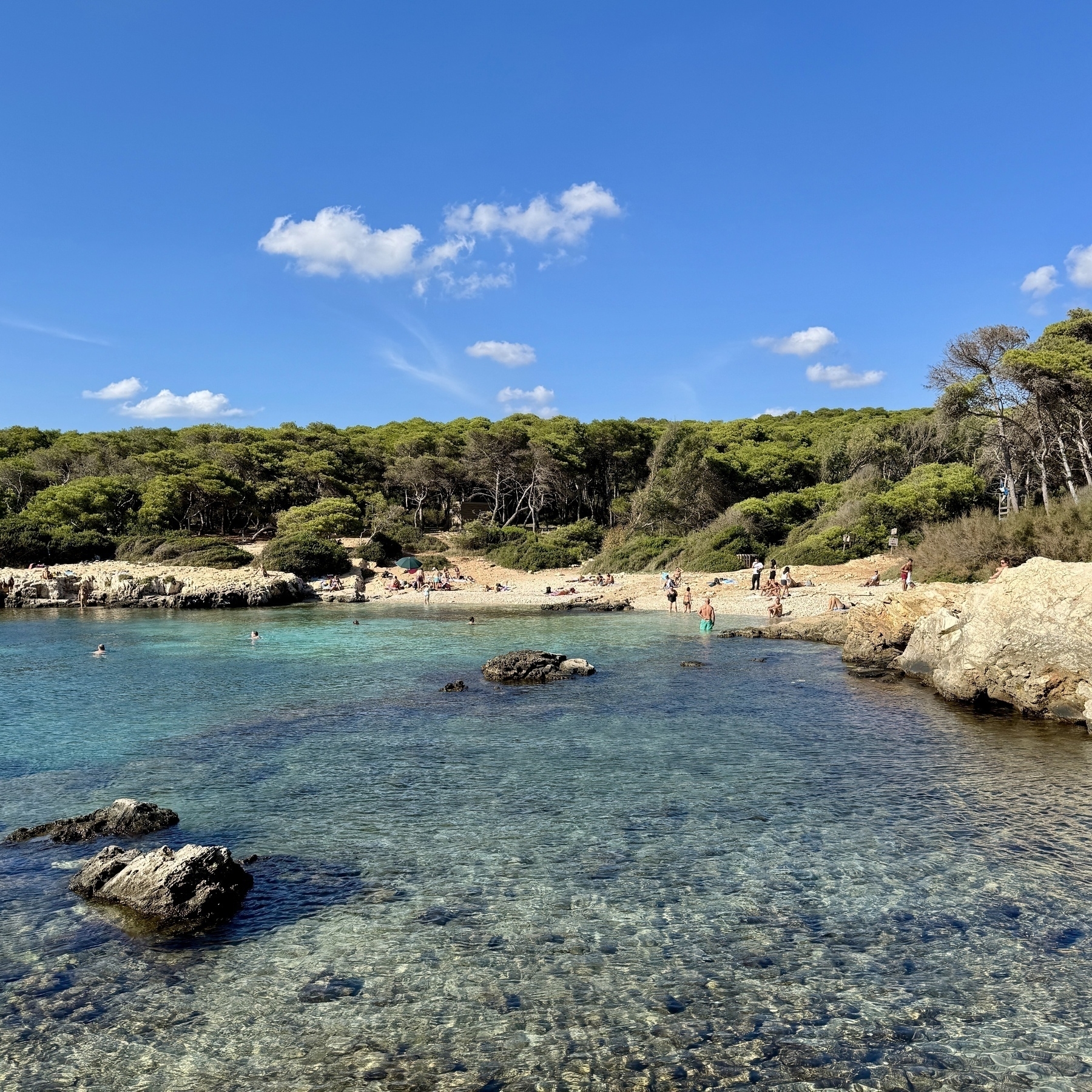 A beach at Porto Selvaggio nature reserve in Salento on a sunny October day, with a handful of people sunbathing and swimming.