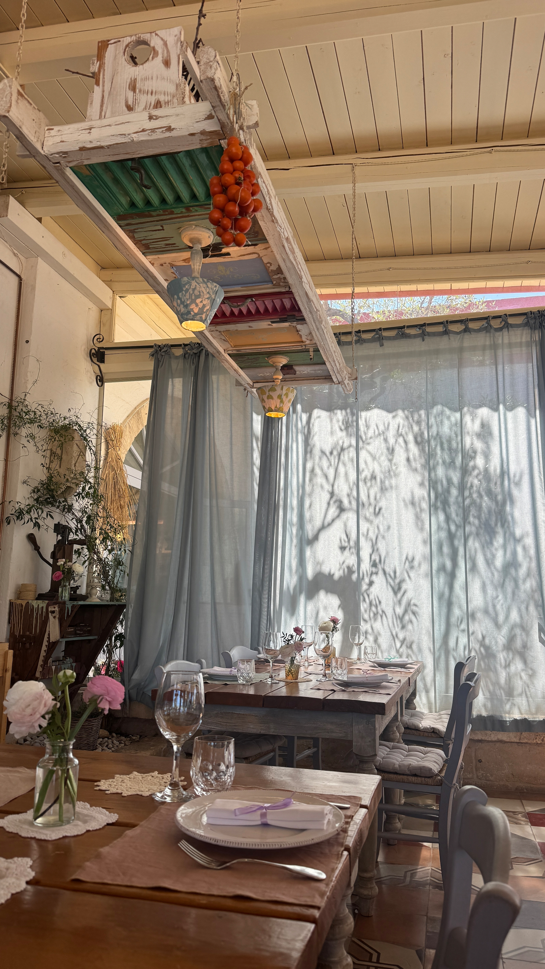 A restaurant in Masseria Montenapoleone in Puglia. There are wood tables, tomatoes hanging from the roof and a light green curtain blocking the sun from entering.