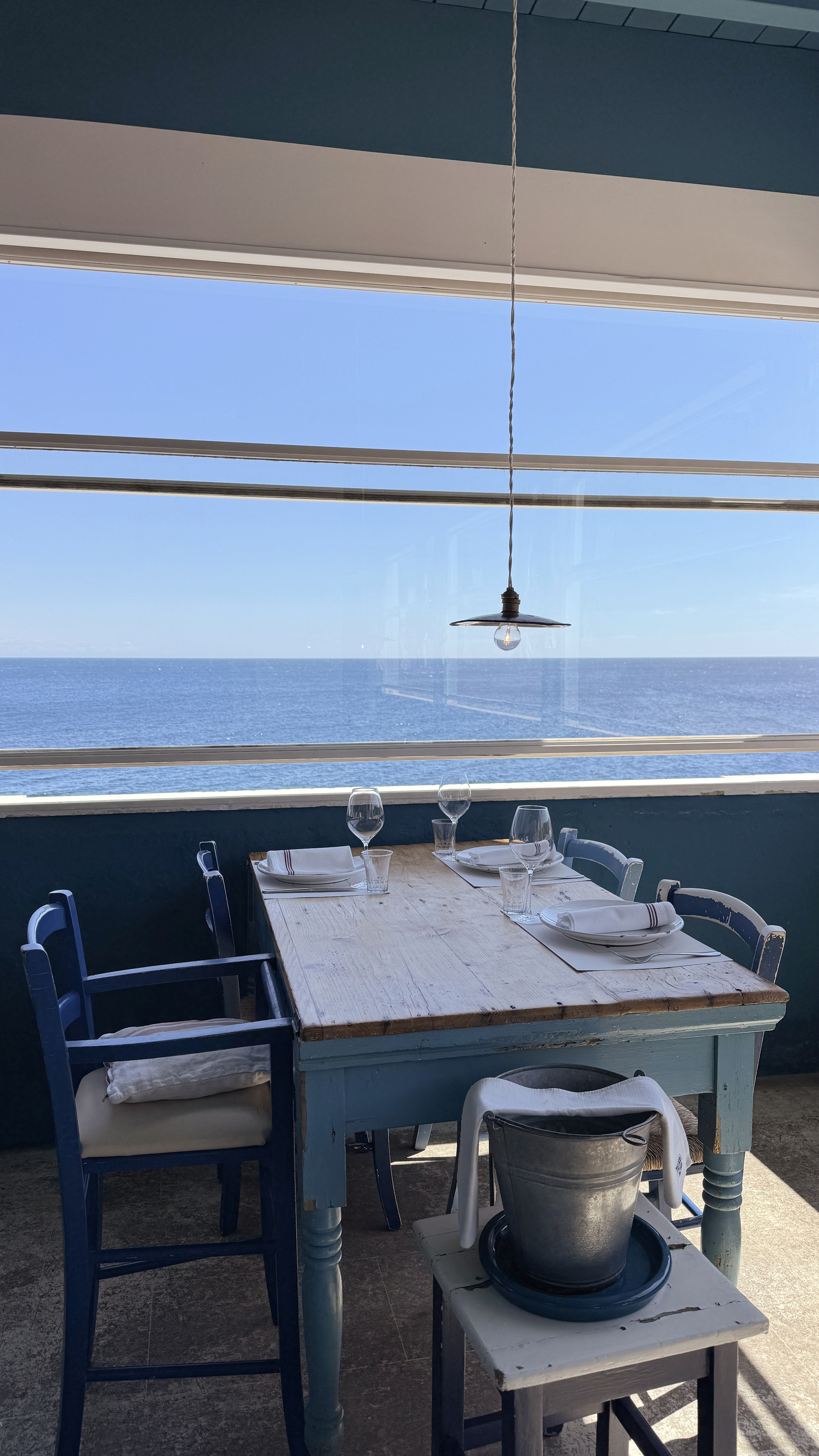 A wooden table in a restaurant with a large window looking over a view of the sea.